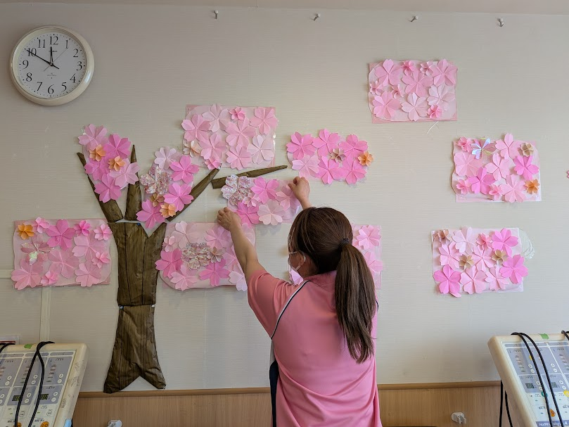 壁面に手作りの桜の装飾を飾りつけるスタッフ